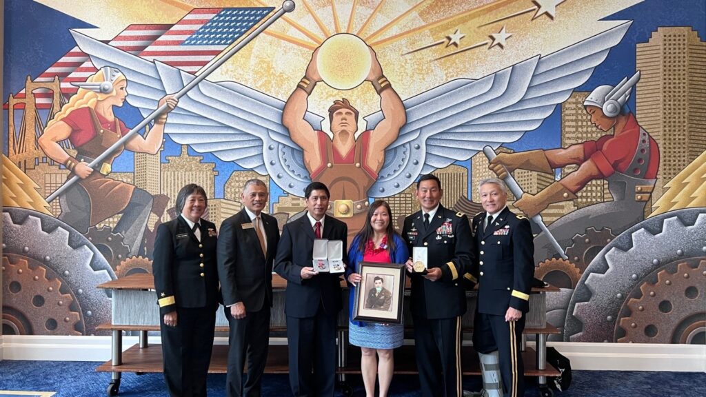 Military officials pose in front of a wall mural following a private ceremony where Ricky Leo received a Bronze Star on behalf of his father Lui Gain Thyn ("Sonny Leo")