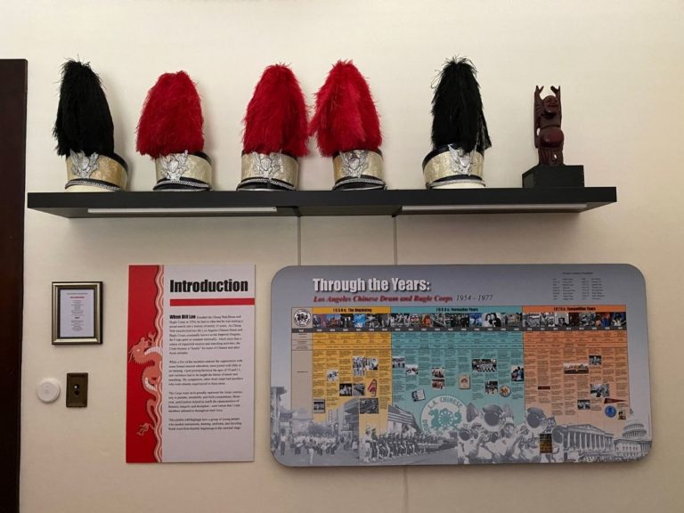 Photo of the Drum & Bugle Display room with a view of the front wall, including 5 hats on a display shelf and information posters underneath